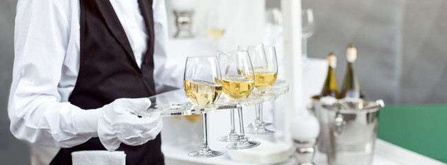 Wall Mural - Midsection of professional waiter in uniform serving wine during buffet catering party, festive event or wedding. Full glasses of champagne on tray.