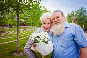 Attractive elderly couple walking around the city with a bouquet of flowers