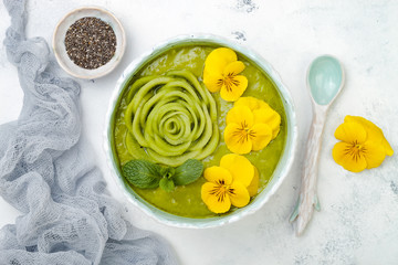 Wall Mural - Breakfast detox green smoothie bowl topped with kiwi rose and edible Pansy flowers. Overhead, top view, flat lay, copy space