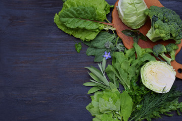 Composition on a dark background of green leafy vegetables containing folic acid, riboflavin, vitamin B9, B2, K, C - cabbage, broccoli, chard, lettuce, spinach, parsley, celery, dill, sage. Top view.