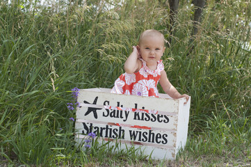 Little toddler girl poses in painted wooden crate in front of grass.