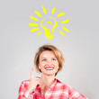 Business woman has an idea. Smiling woman looking up and showing finger up on light bulb over her head