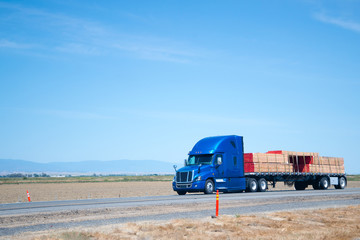 Wall Mural - Big rig blue semi truck with flat bed trailer transporting lumber wood on flat road