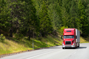 Wall Mural - Modern red semi truck with dry van trailer driving on road with green trees forest on the roadside hills