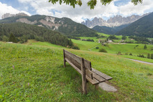 Wooden Public Garden Seat With No People With An Italian Small Mountain Town In Dolomites As Background