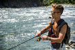 © starsstudio - Young handsome male tourist standing and fishing in river in sunny day with rod
