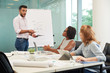 © DragonImages - Portrait of handsome bearded entrepreneur standing at marker board and motivating sales managers to exceed goals during working meeting