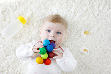 Wall Mural - Cute baby girl playing with colorful wooden rattle toy, nursing bottle and dummy