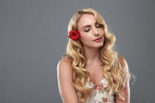 Portrait Of Gorgeous Blond Woman With Flower In Hair Posing Elegantly With Eyes Closed Against Grey Background