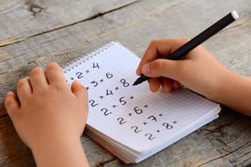 Child solves math examples. Child holds a marker in his hand and writes answers to multiplication examples in a notebook. Learning multiplication table concept 