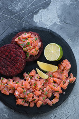 Wall Mural - Salmon tartar with beetroot cutlets served on a stone slate, flat-lay on a grey stone background