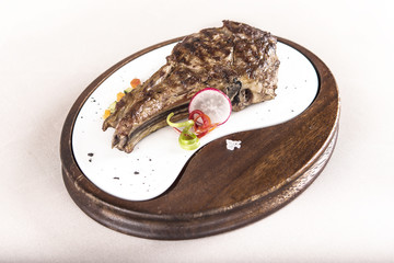 Succulent grilled large t-bone steak garnished with herbs, radish and salt, on a white plate; brown background