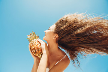 Wall Mural - Summer portrait of young woman having fun with pineapple outdoors