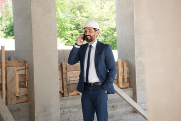 smiling middle aged contractor talking on smartphone at construction site