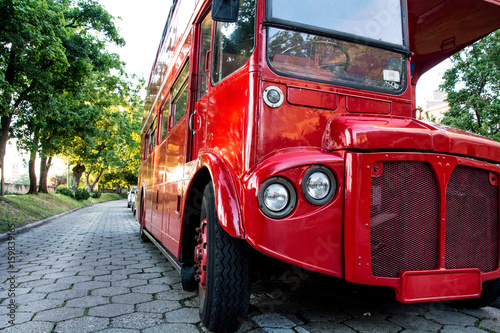 Red two-story English bus standing in the park on the waterfront Poster