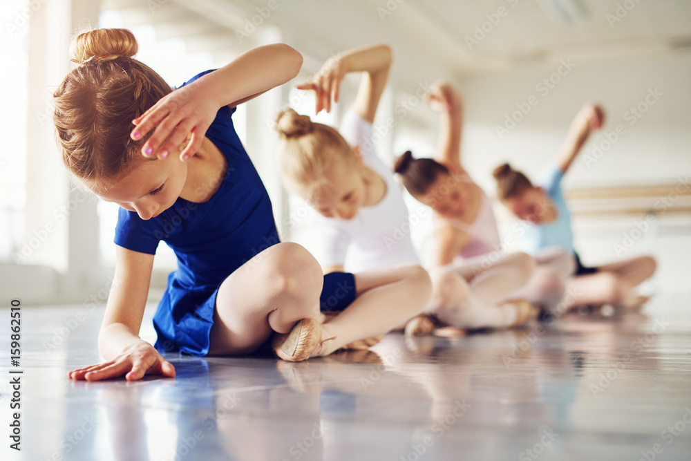 Girls bending sitting on floor in ballet class - obrazy, fototapety, plakaty 