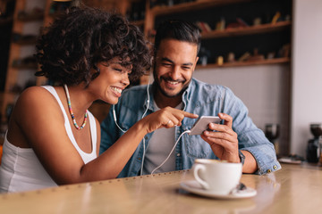 Wall Mural - Smiling couple at cafe using smart phone