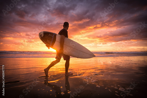 Fototapety Surfing  surfer-biegajacy-po-plazy-o-zachodzie-lub-wschodzie-slonca