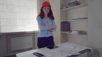Aufkleber - Redheaded engineer at work using digital tablet. Professional female looking at the camera with arms crossed. On the desk sketch with technical drawing some building.