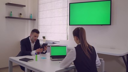 Poster - Adult handsome worker wearing elegant suit using digital tablet showing presentation or new design project. On the desk laptop with green screen. Back view on the businesswoman