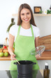 © rogerphoto - Young happy woman in a green apron cooking in the kitchen. Housewife found a new recipe for her soup. Healthy food and vegetarian concept