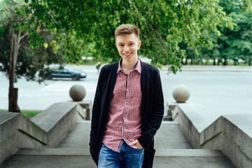 Portrait of young handsome trendy smiling man in plaid shirt in the city looking at camera, outdoors