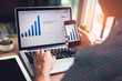 © Mymemo - Young man working from home using smartphone and laptop computer, Asian businessman holding using mobile smart phone and notebook pc checking business revenues online