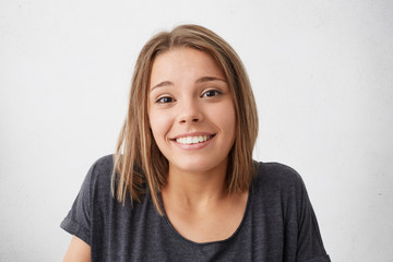 Wall Mural - Magnificent pretty woman with dark narrow eyes and pleasant smile shrugging her shoulders having nice and doubtful look while posing against white background. Impressive female with beautiful face