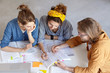 © WHstudio Leushin N - Two pupils working with their tutor doing home assigment sitting at white table. Three college students working with books underline important information on pages having deep look. Scientific work