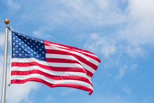Large American Flag Waving On Flag Pole With Cloud Blue Sky. Windy And Sunny Day With Waving Star And Striped Flag Blowing/flowing. Ruffled USA Flag. Room For Text.