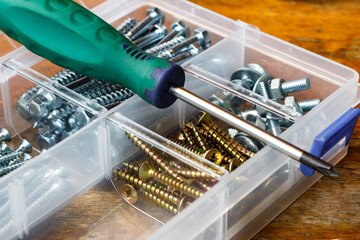 Screws and bolts in the storage box with screwdriver on the workbench