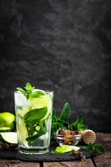 Wall Mural - Refreshing mint cocktail mojito with rum and lime, cold drink or beverage with ice on black background