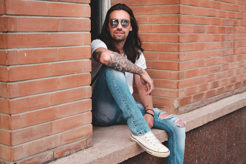 Wall Mural - Stylish hipster model with long hair lifestyle in the street. Dressed in a white T-shirt and torn blue jeans in the city