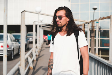 Wall Mural - Stylish hipster model with long hair lifestyle in the street. Dressed in a white T-shirt and torn blue jeans in the city