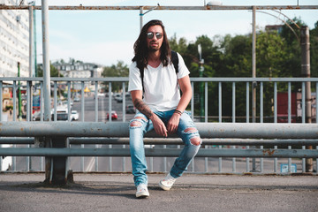 Wall Mural - Stylish hipster model with long hair lifestyle in the street. Dressed in a white T-shirt and torn blue jeans in the city