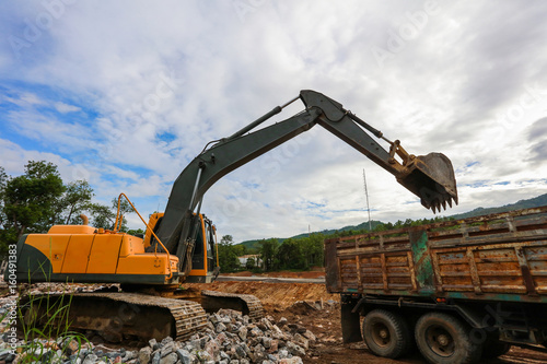 Fototapeta Ekskawator lub backhoe przy budową z niebieskim niebem i zmierzchem, ciężkim przemysłem i bezpieczeństwem przy pracy pojęciem ,.