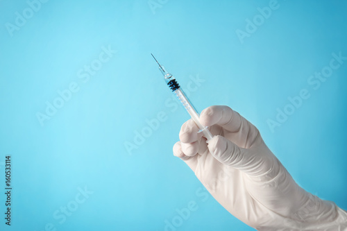 Leinwand Poster  Hand of nurse with syringe prepared for vaccination, on color background