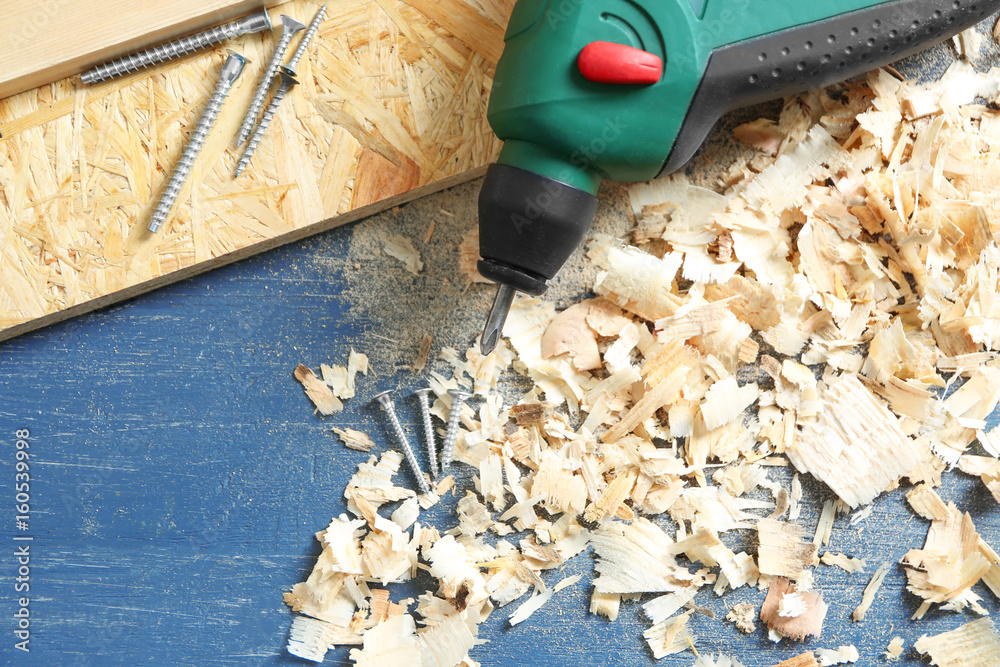 Drill, screw nails, wooden boards and saw dust on table in carpenter's workshop