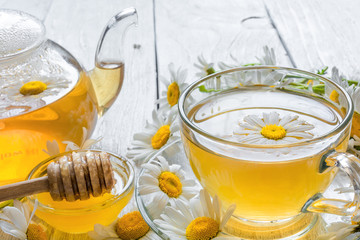 cup of herbal tea with chamomile flowers and honey and teapot