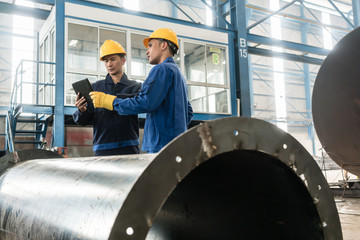 Asian experts checking information on tablet PC while supervising work in a modern factory