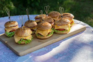 Tasty burgers with cheese, lettuce, onion and tomatoes served outdoor on a wooden table