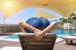 Woman enjoying and relaxing on deck chair by the pool. Sunbath and sunny day at beach resort. Summer and holiday concept
