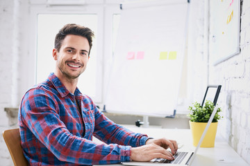 Succesful young web designer, programmer working on laptop in start-up office