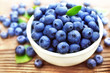 Bowl of fresh ripe sweet juicy blueberries with leaves on wooden background