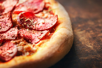 Pizza with pepperoni and salami on a rustic wooden table macro image.