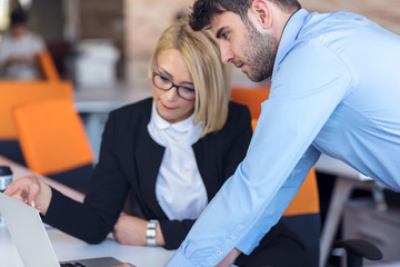 Colleagues chatting, sitting together at office table, smiling