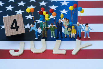 Wall Mural - miniature people, happy american family holding balloon and wooden block and alphabet as 4 July with United State national flag in the background as celebrating the Independence day