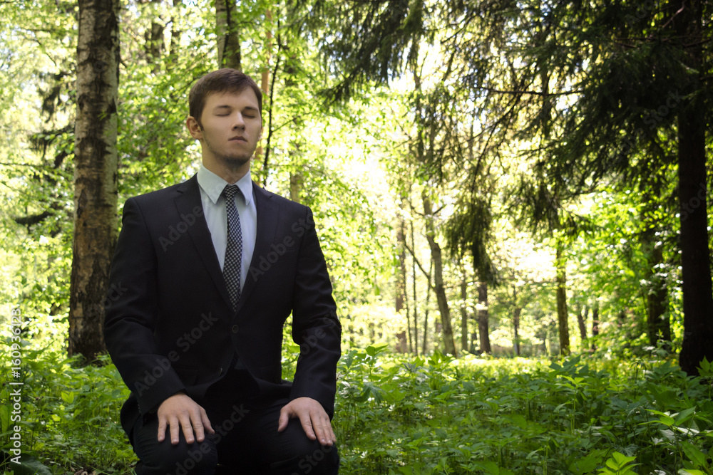 Businessman meditating in nature. A man in a business suit sits in the ...