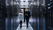 © Gorodenkoff - Caucasian Male and Asian Female IT Technicians Walking through Corridor of Data Center with Rows of Rack Servers. They Have Discussion, She Holds Tablet Computer.