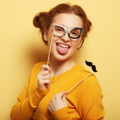 Young woman with  fake mustaches and glasses over yellow backgro